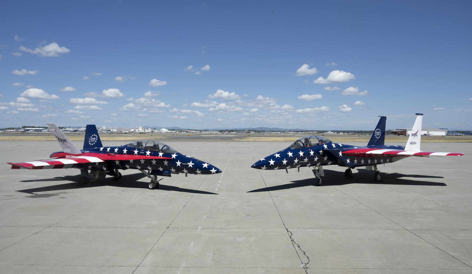 Two red, white and blue jet aircraft are sitting on the ramp ready for takeoff. The body of the aircraft is painted in blue with white stars, and the wings are red and white stripes to mirror the American flag.