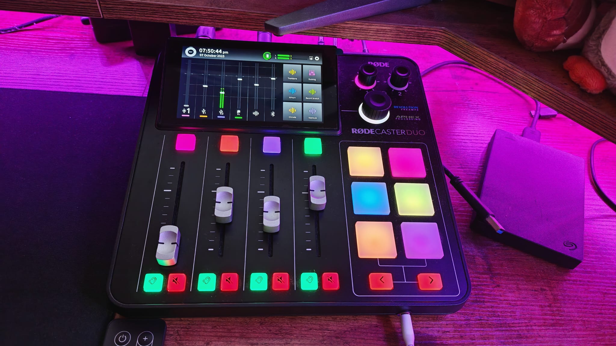 Pembe RGB aydınlatma altında bir oyun masasında RodeCaster Duo