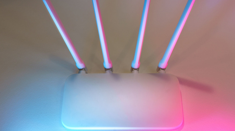 Pembe ve mavi ışıklarla aydınlatılmış beyaz bir router masada duruyor