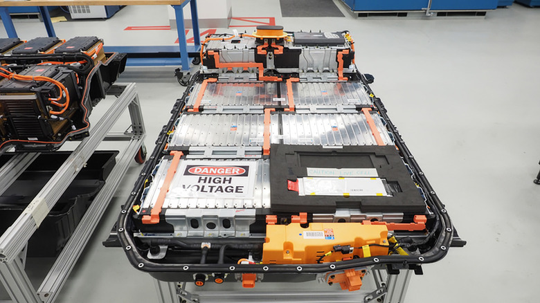 EV batteries in a factory. "Danger: High Voltage" on one of them.